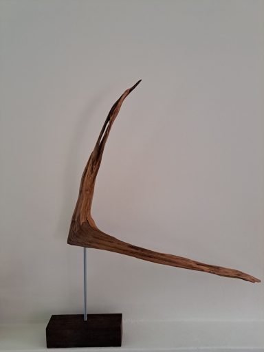 Zwaluw 45 Euro Abstract houten sculptuur met een lange, scherpe punt op een zwart voetstuk.