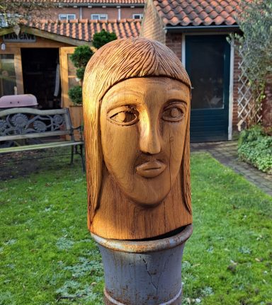 Kop 450 Euro Houten sculptuur van een hoofd met een rechte neus en rechtopstaande haarstijl.