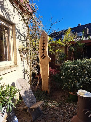 Zonnevanger VERKOCHT Houten sculptuur in een tuin met planten en zonlicht.
